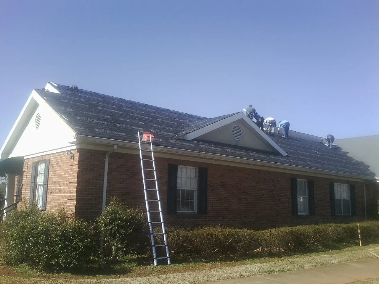 Crew tearing shingles off a brick ranch roof with a ladder set — Emergency Roof Repair work by our crew in Elmaton