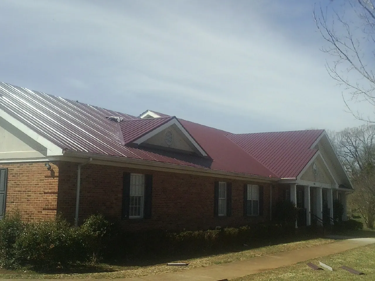 Red metal roof with gabled entries on a long brick building, from a Hail Damage Roof Repair job in Elmaton