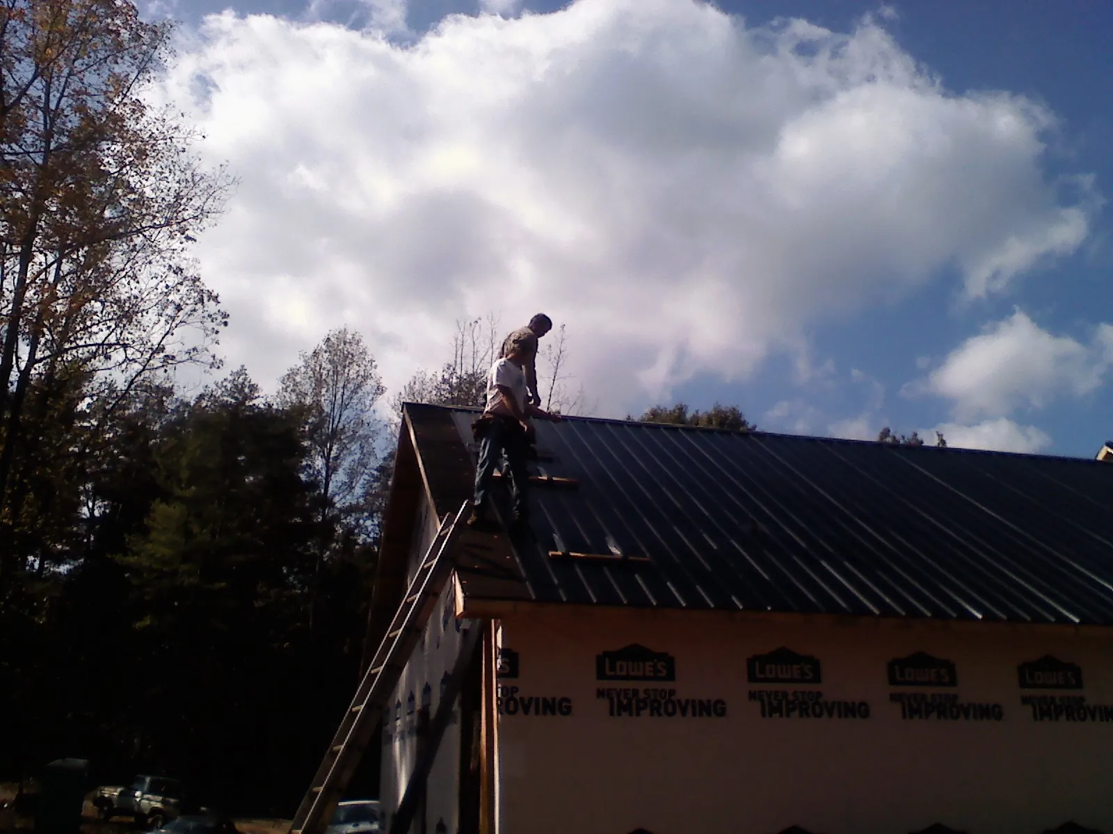 Roofer fastening dark metal panels high against a cloudy sky, from a Roof Inspection job in Elmaton